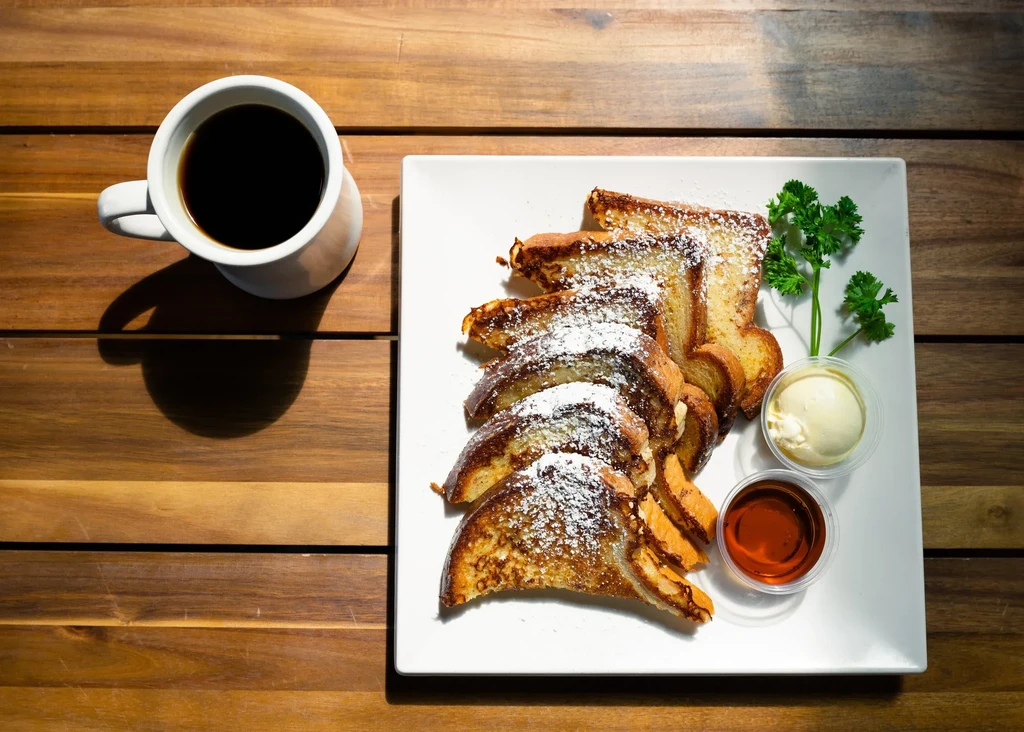 French toast with powdered sugar, syrup, butter, parsley, and coffee.