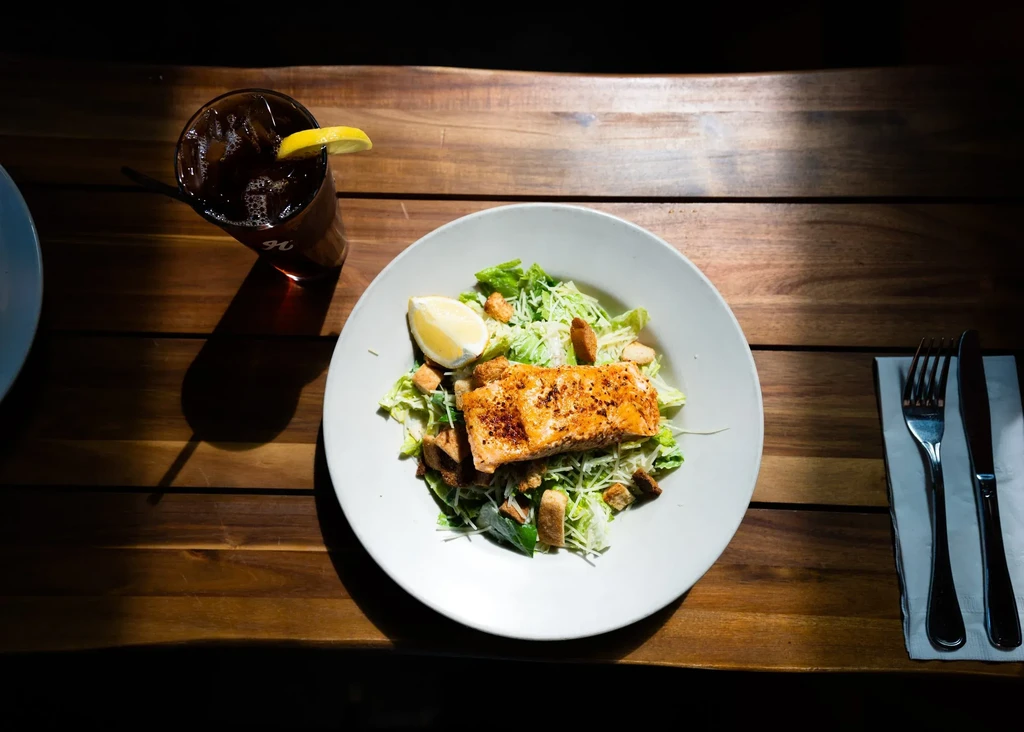 Overhead: Caesar salad with grilled salmon, iced drink, and cutlery.