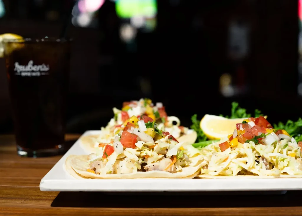 Three fish tacos with salsa, lemon, and a dark beverage.