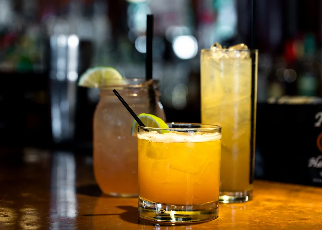Three cocktails on a reflective wooden bar, garnished with lime.
