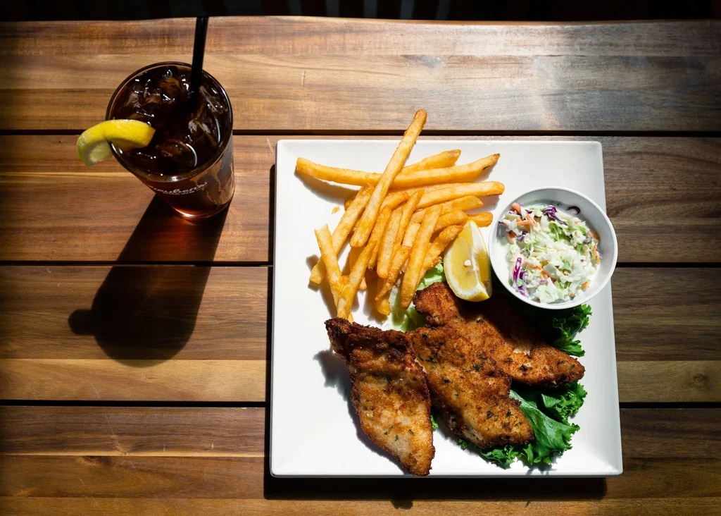 Fried fish, fries, coleslaw, and iced drink meal on wooden table.