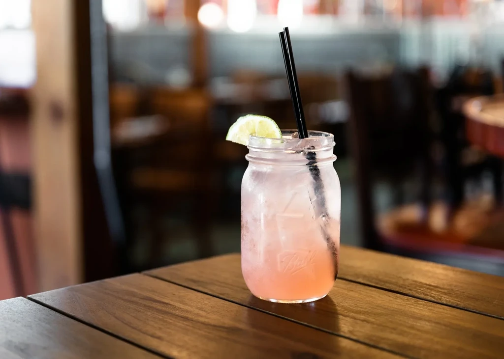 Frosty pink drink in Ball mason jar with lime on wooden table.
