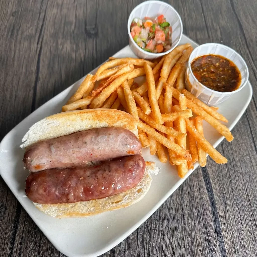 Overhead view: sausage sandwich, fries, salsa, and dark sauce on a plate.