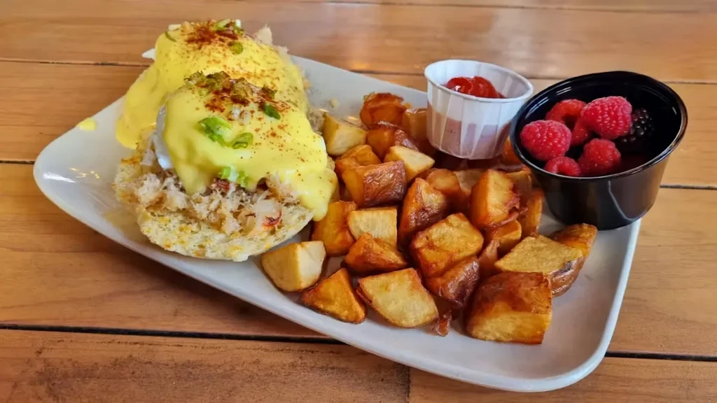 Close-up of crab Eggs Benedict, home fries, ketchup, and mixed berries.