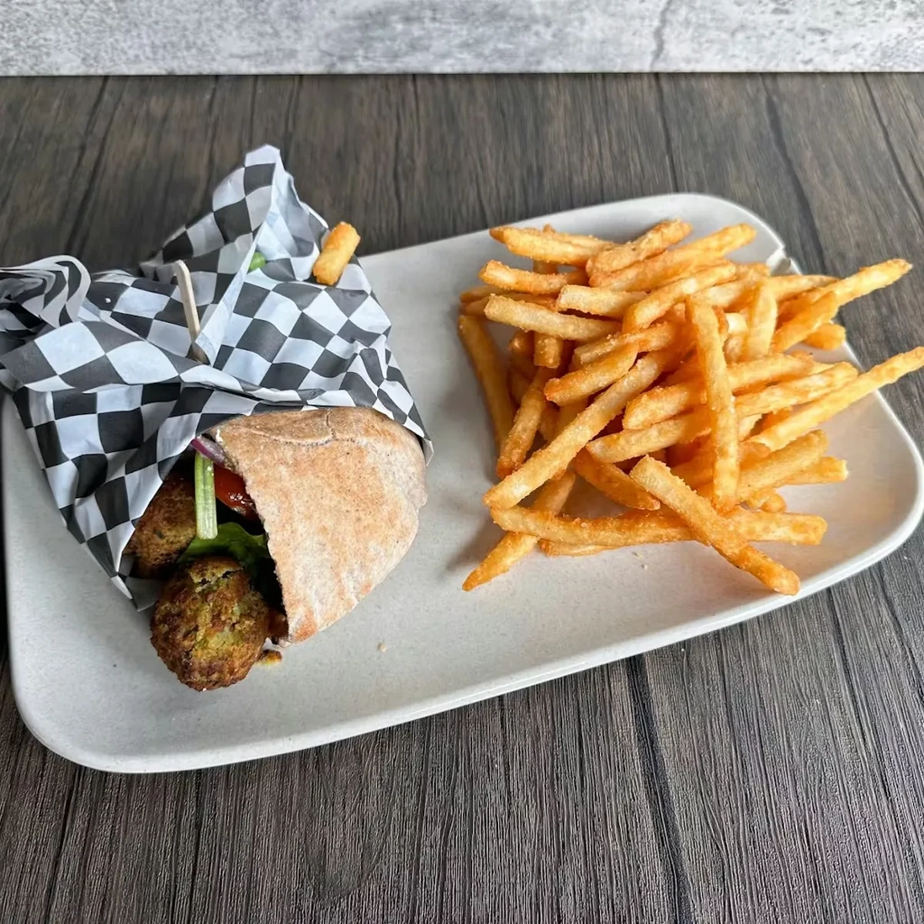 Close-up of falafel pita sandwich and french fries on a plate.