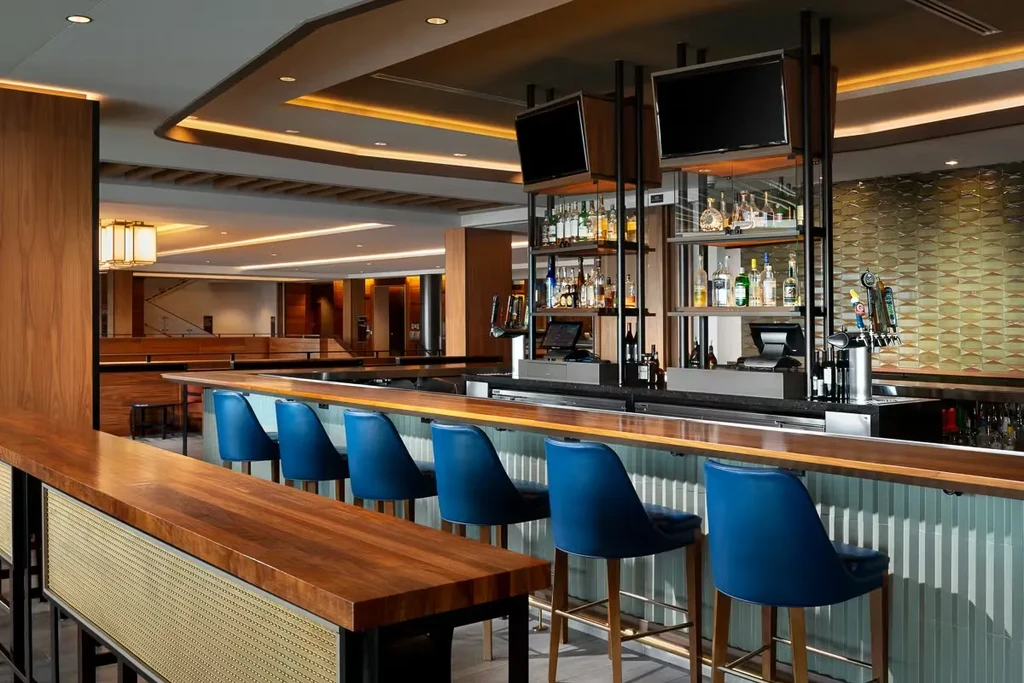 Modern bar with polished wood counter, blue stools, and liquor shelves.