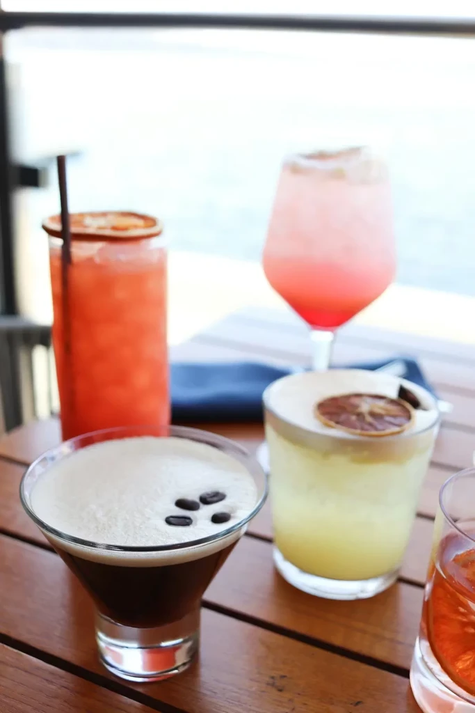 Four colorful cocktails, including espresso martini, on an outdoor wooden table.