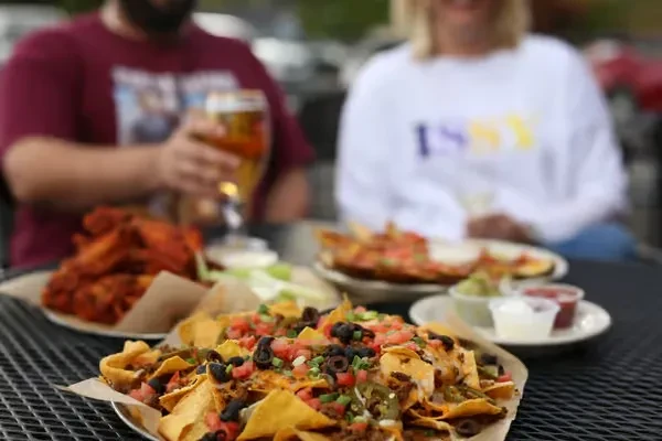 Loaded nachos, buffalo wings, and dips on an outdoor table.