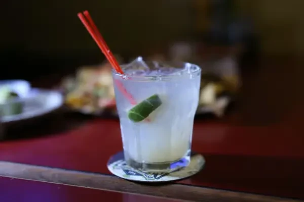 A cocktail with ice, lime, and red straws on a bar counter.
