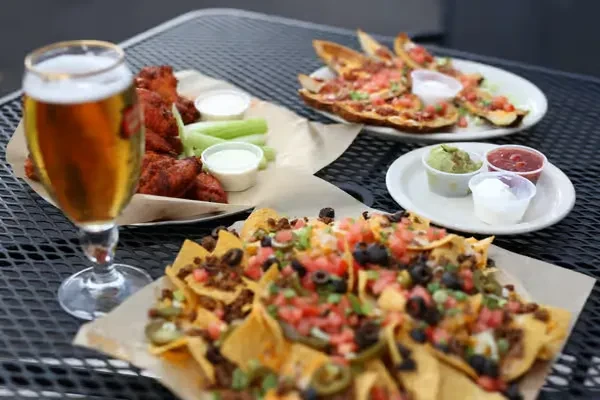 Overhead view of nachos, buffalo wings, beer, and dips on a table.