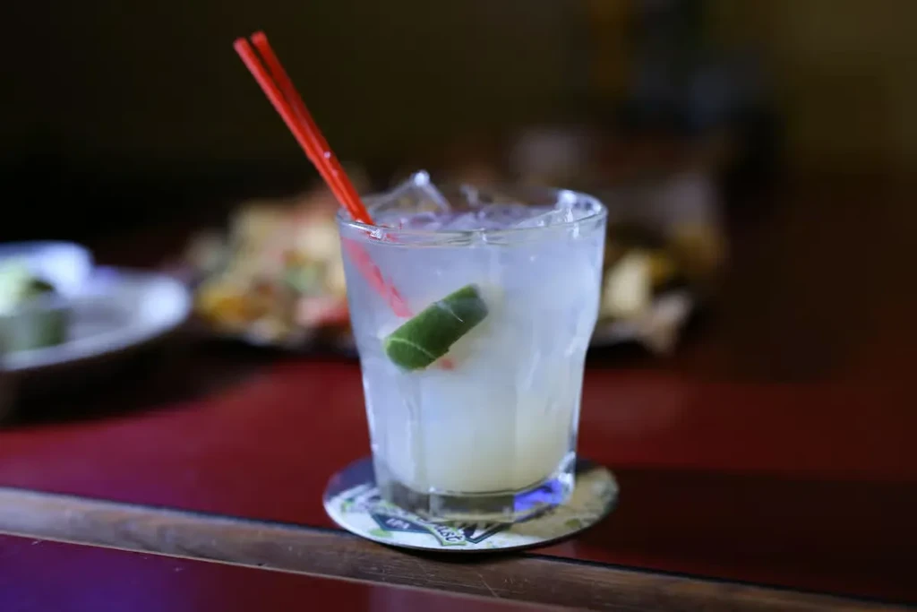 Glass of iced drink with lime and red straws on bar.