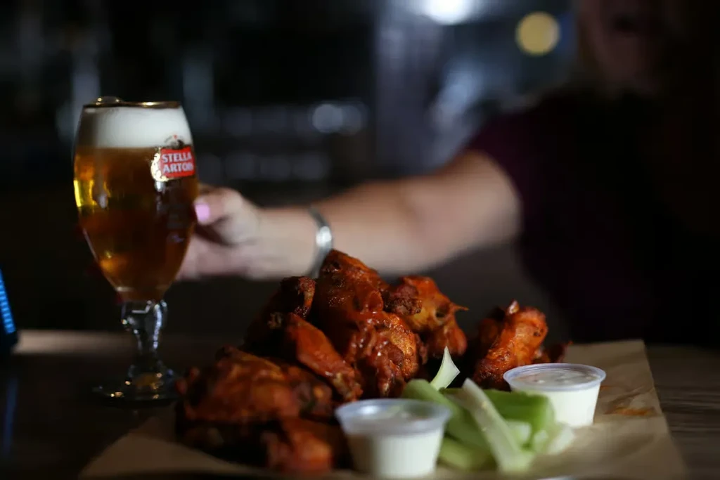 Buffalo wings, celery, dipping sauce, and glass of Stella Artois beer.