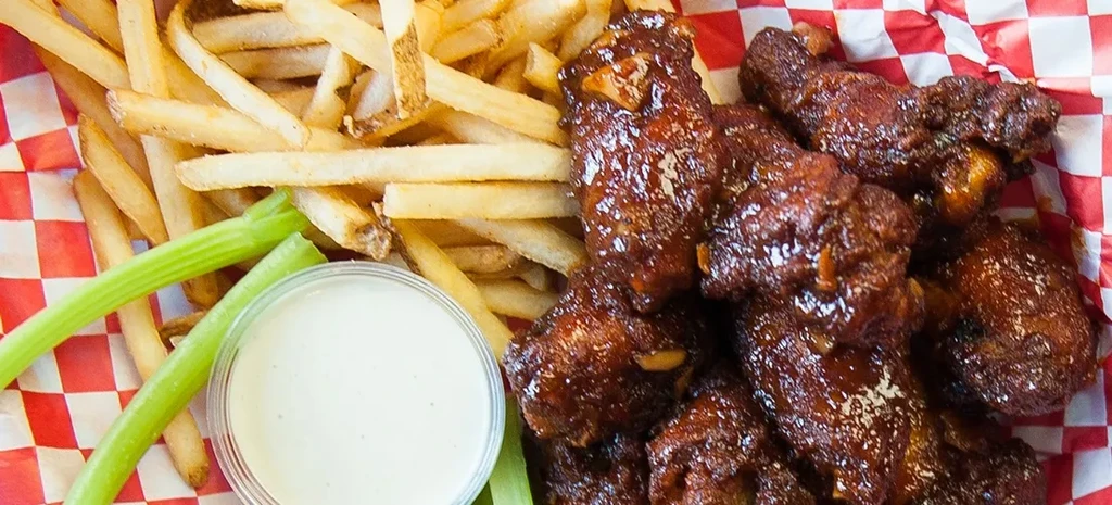Overhead basket of sauced chicken wings, fries, celery sticks, dipping sauce.