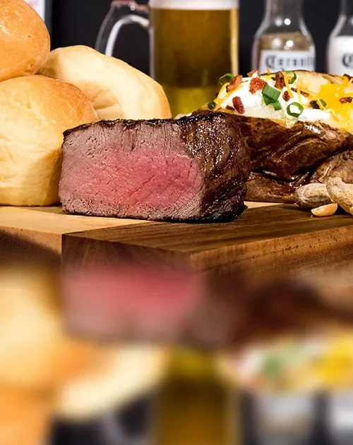 Medium-rare steak, bread rolls, loaded baked potato, and beer.