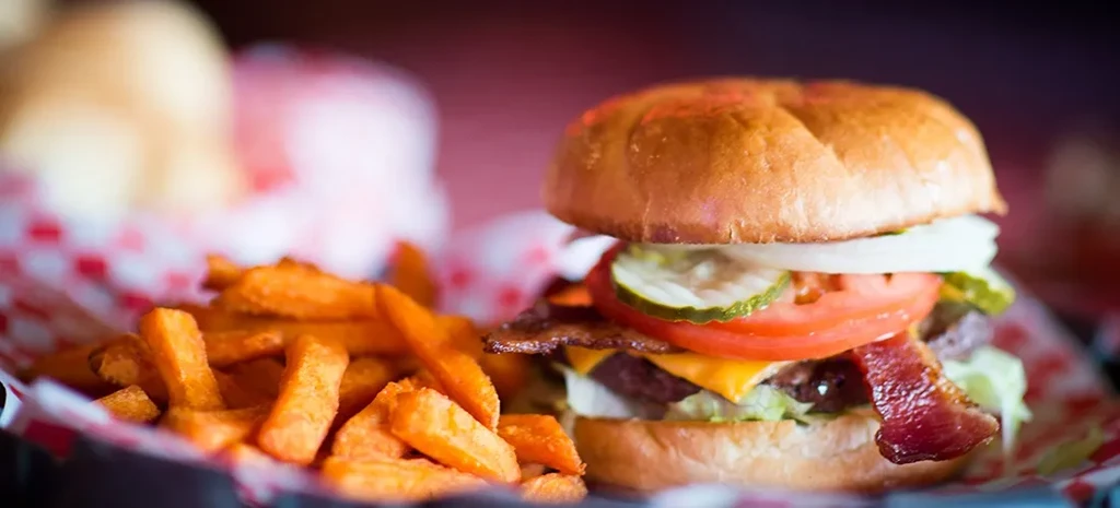 Gourmet burger with bacon, cheese, and sweet potato fries in a basket.