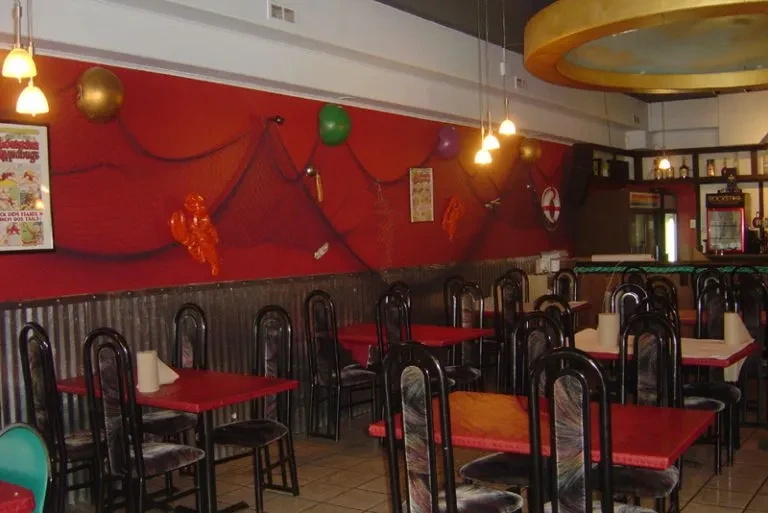 Empty casual restaurant interior with red tables, walls, and nautical decor.