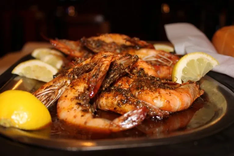 Cooked shrimp with seasoning and lemon slices on a dark platter.