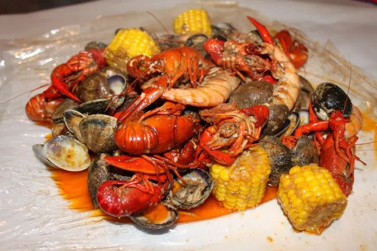 Overhead seafood boil with crawfish, shrimp, corn, and spicy sauce.