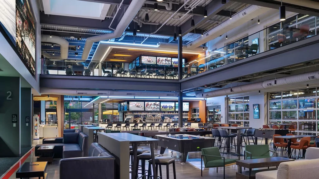 Modern industrial-chic multi-level sports bar with diverse seating and TVs.