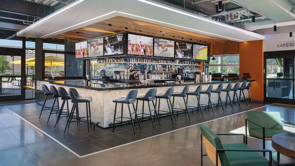 Modern, spacious sports bar with L-shaped bar and multiple screens.