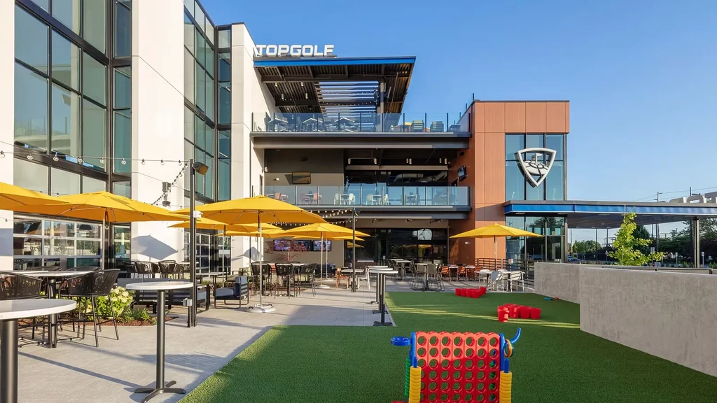 Exterior view of a modern Topgolf venue with patio and lawn games.