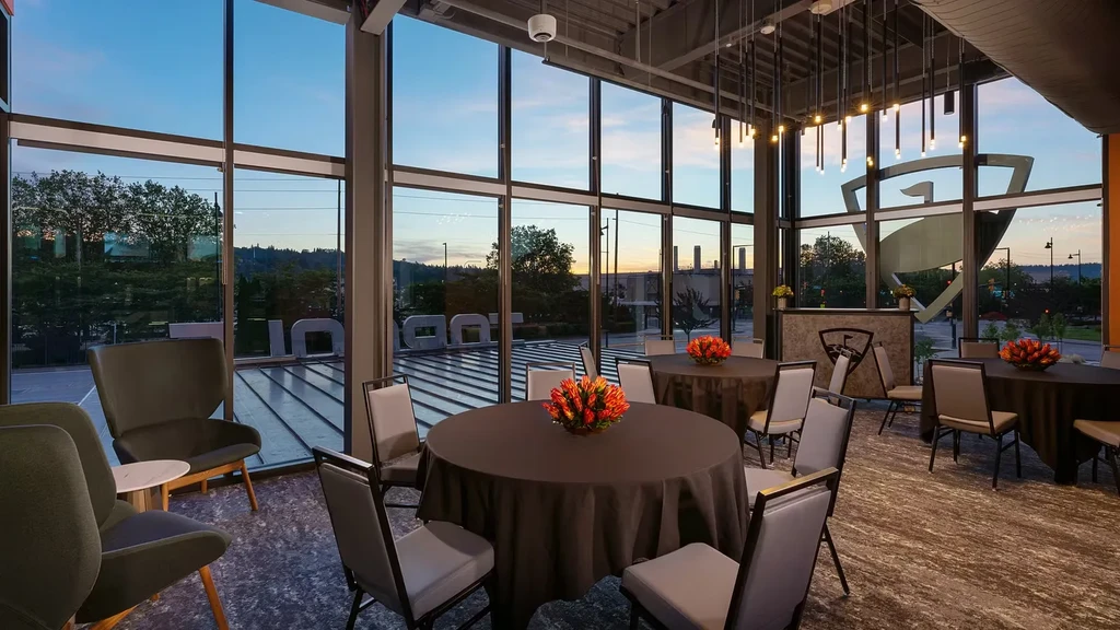 Modern Topgolf event space with tables and large windows at sunset.