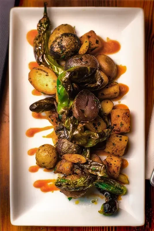 Professionally plated roasted vegetables with orange sauce on a white plate.