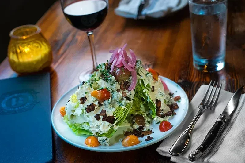 Wedge salad with blue cheese, bacon, tomatoes, and pickled onions.