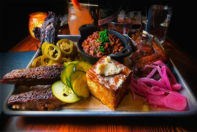 Hearty barbecue platter featuring ribs, wings, cornbread, beans, and pickled vegetables.