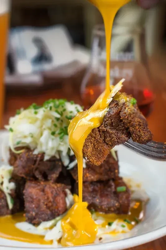 Fork lifts crispy meat, golden cheese sauce pours over cabbage stack.