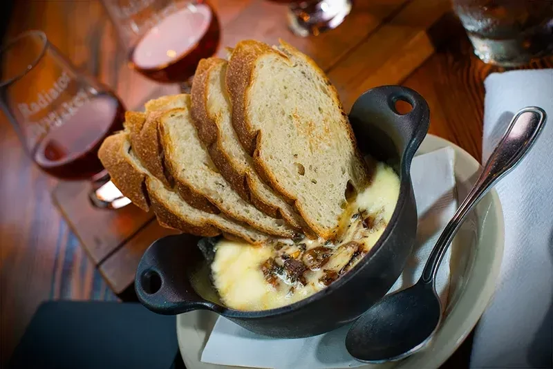 Cast iron pot of melted cheese dip, herbs, and toasted rustic bread.
