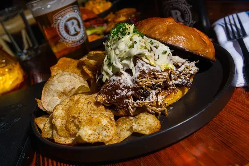 Close-up of pulled pork sandwich with coleslaw, chives, and chips.
