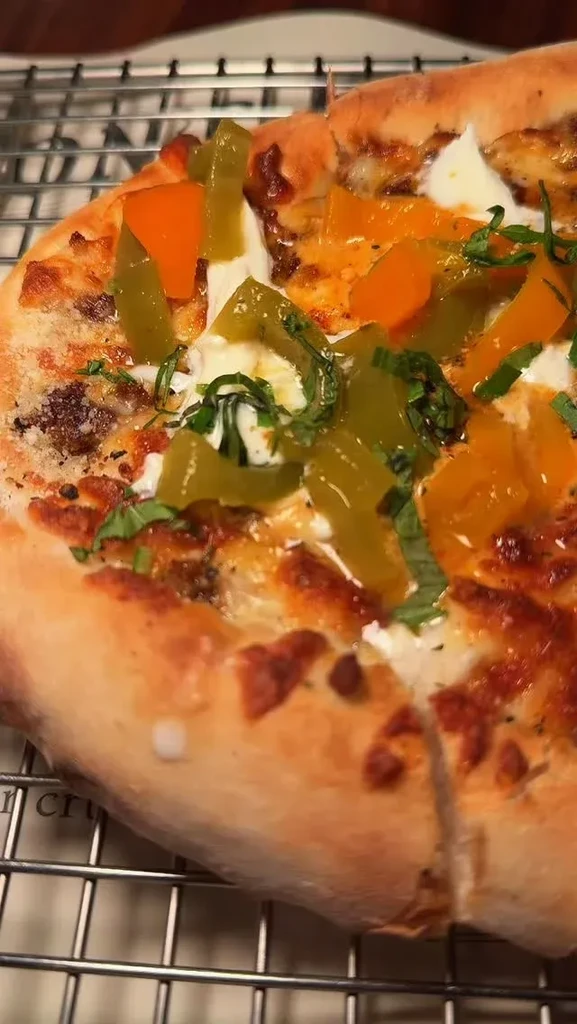 Personal pizza with colorful peppers, cheese, herbs, and meat on a rack.