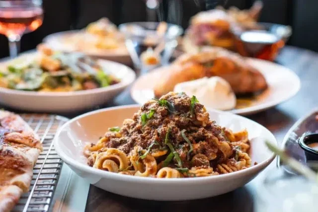 Restaurant table with pasta, flatbread, salad, meat, and drinks.