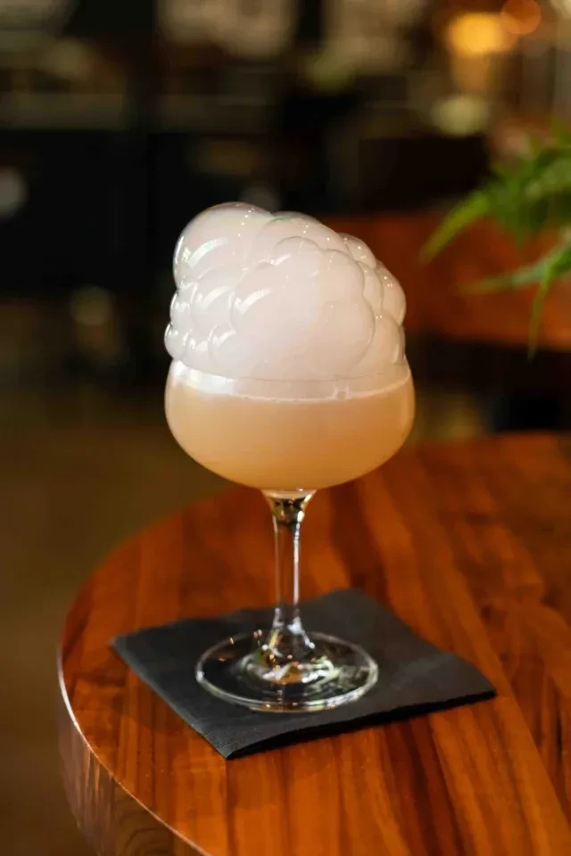 Pale peachy-beige cocktail with dense white foam in a coupe glass.