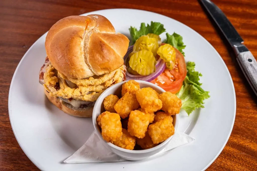 Burger topped with onion rings, tater tots, and side salad.