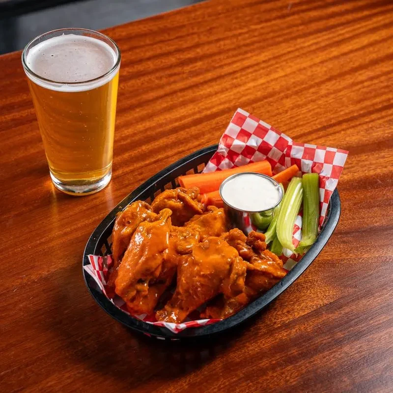 Orange buffalo wings, vegetables, dip, and a pint of beer.