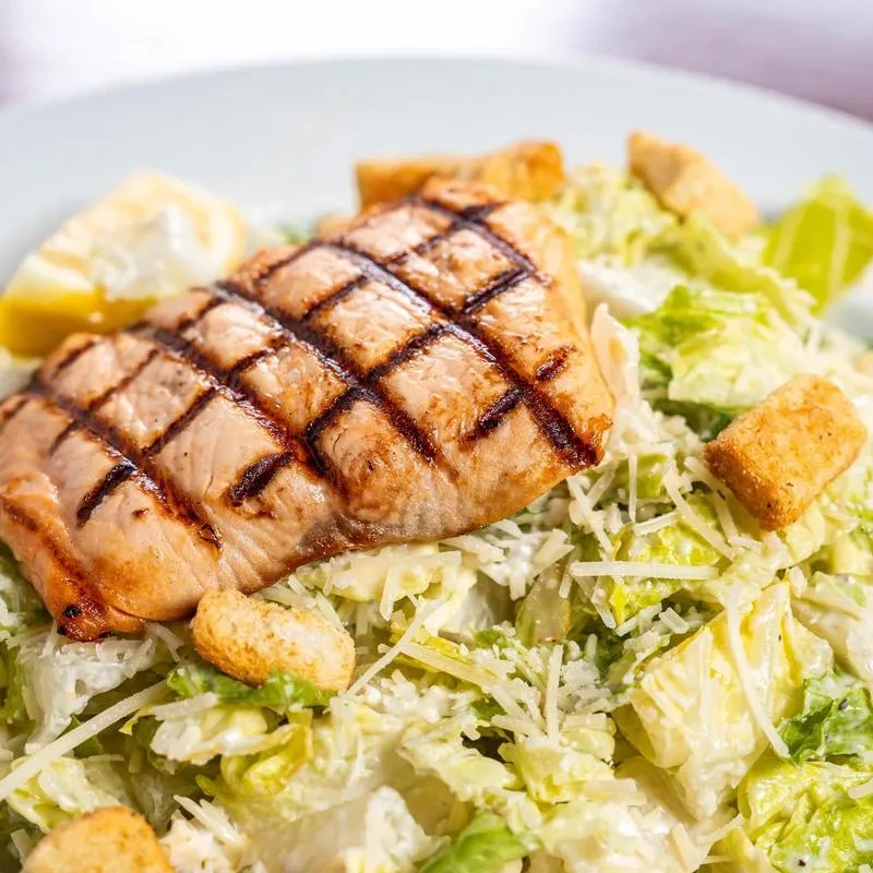 Grilled salmon Caesar salad with lemon, croutons, and Parmesan.