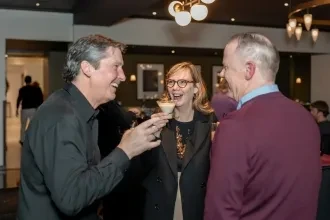Woman laughs with two smiling men in a modern bar.