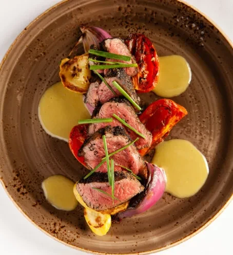 Plated medium-rare steak with roasted vegetables, sauce, and chives.
