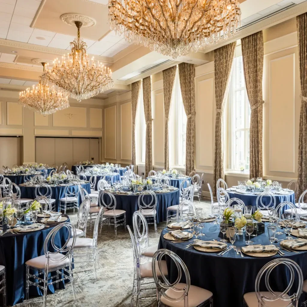 Formal ballroom set with blue tables, acrylic chairs, and chandeliers.
