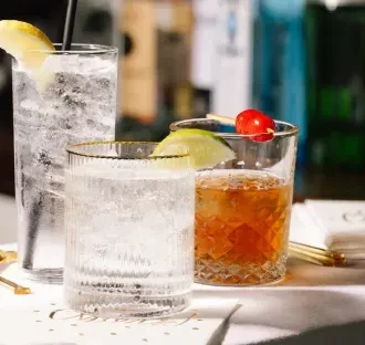 Three garnished drinks in various glasses on a bar.