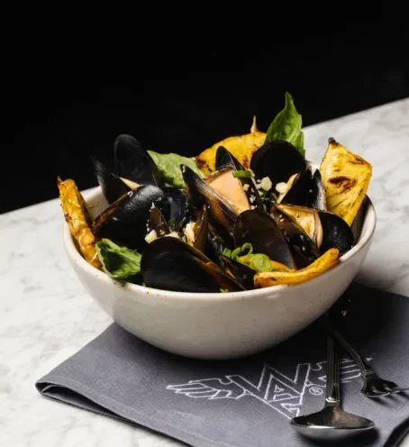 White bowl of mussels, basil, green onions, and grilled bread.