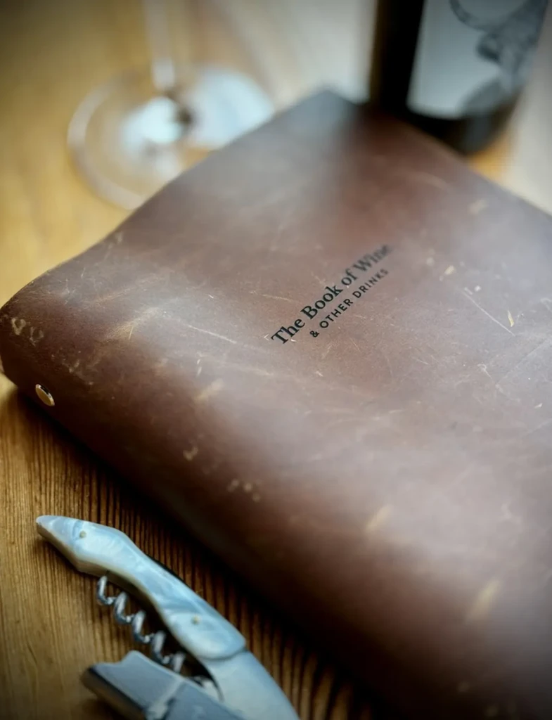Distressed leather book 'The Book of Wine & Other Drinks', with corkscrew.