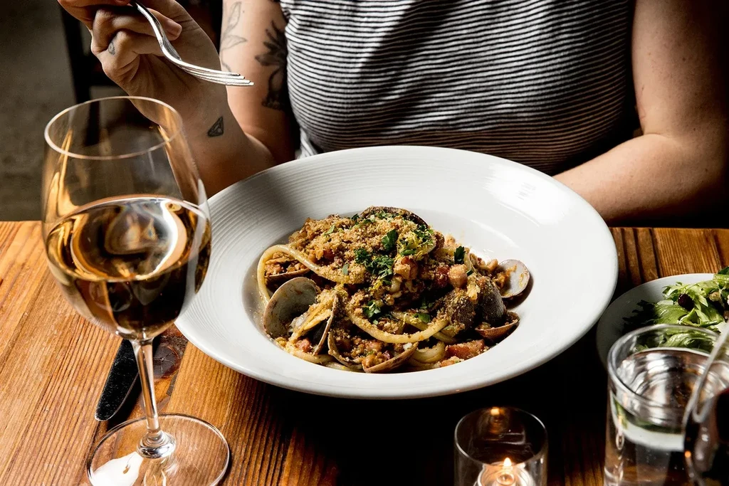 Close-up: pasta with clams and herbs, white wine, person with fork.