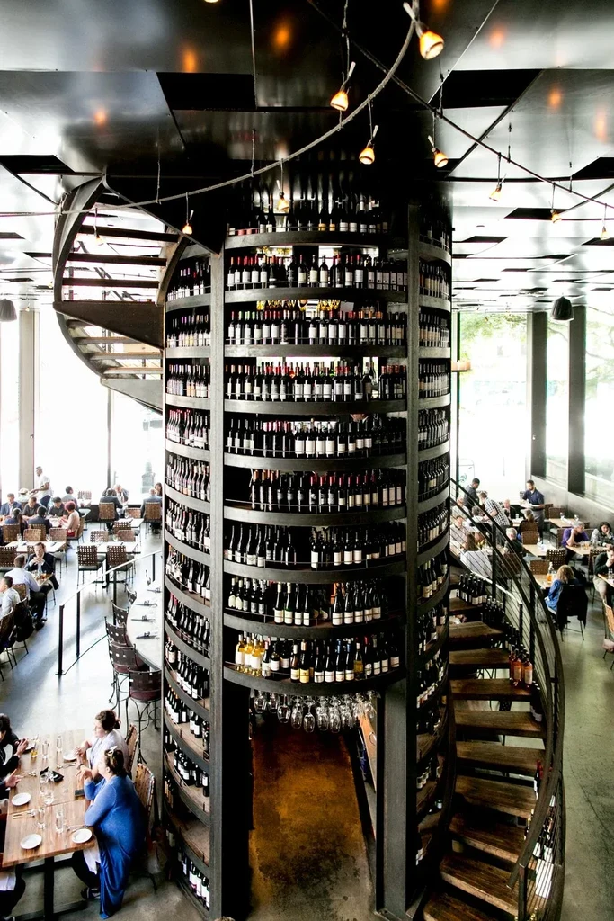Multi-level restaurant with a towering wine rack and spiral staircase.