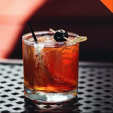 Cold amber cocktail with ice, cherry, and straw in a rocks glass.