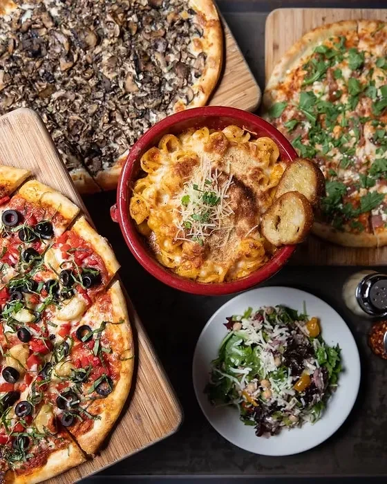 Assortment of Italian pizzas, baked pasta, and fresh salad on a dark table.