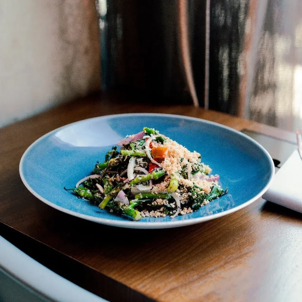 Broccolini salad with red onion and toasted crumbs on blue plate.