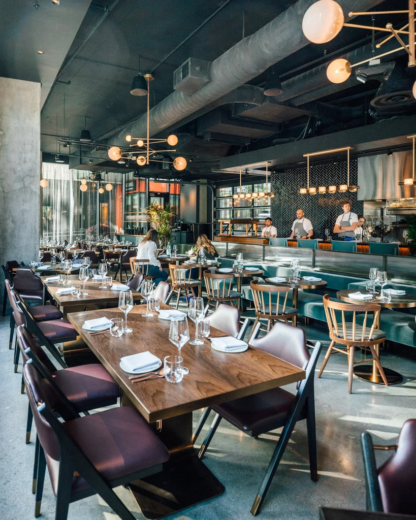 Modern industrial-chic restaurant interior with open kitchen and warm lighting.